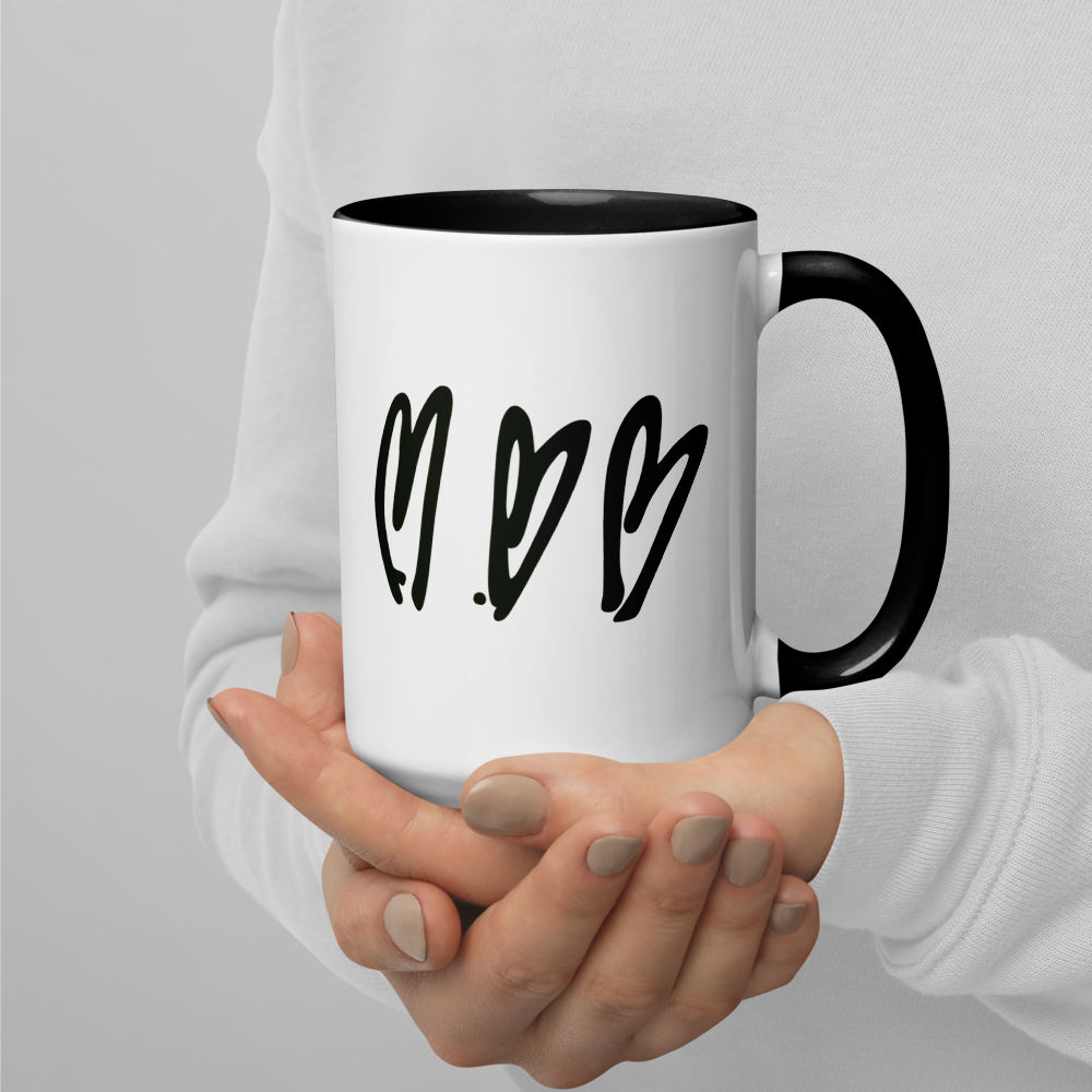 Person holding a white mug with black handles and heart designs on a light gray background