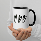 Person holding a white mug with black handles and heart designs on a light gray background