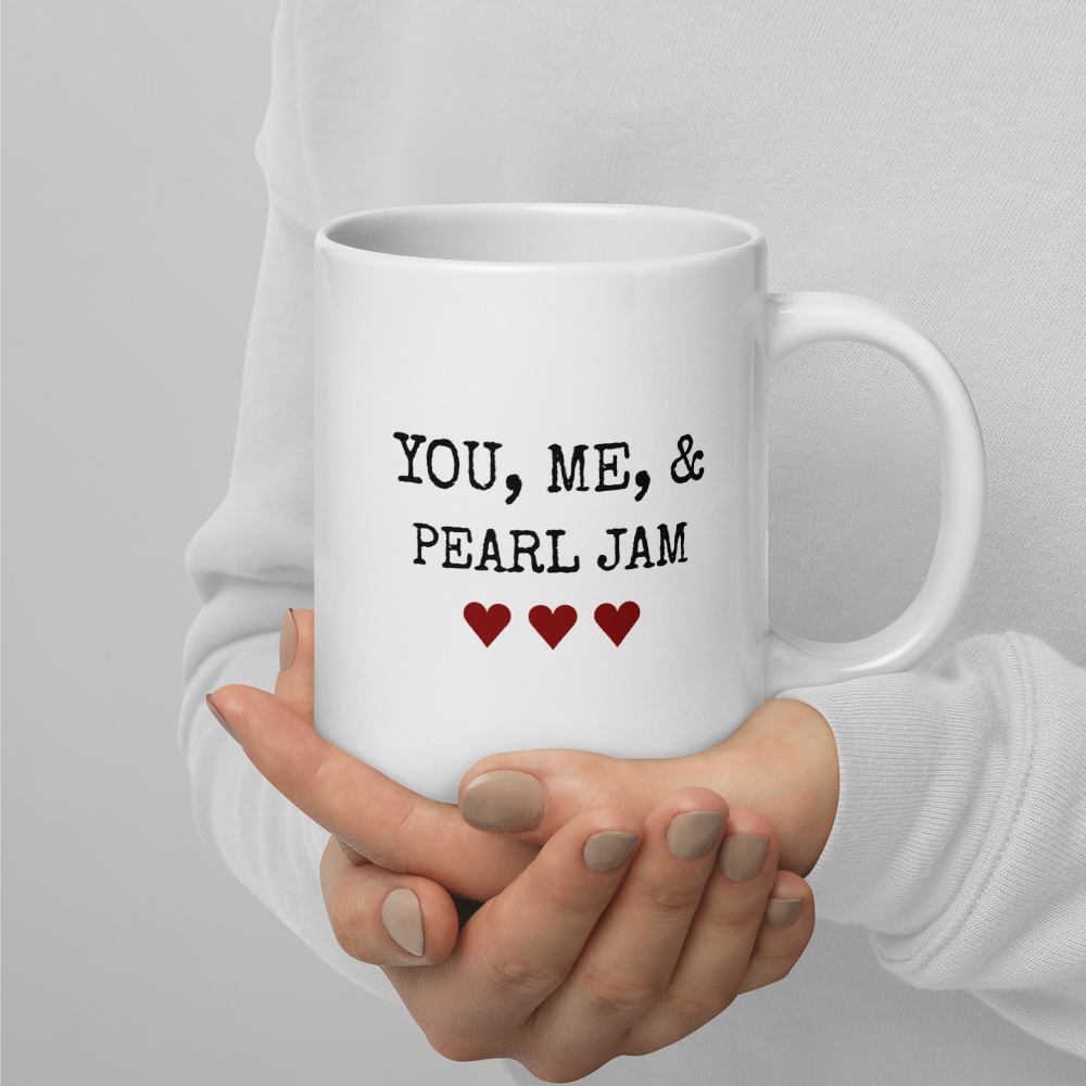 White mug with 'YOU, ME, & PEARL JAM' text held by a person wearing a white sweater.