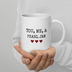 White mug with 'YOU, ME, & PEARL JAM' text held by a person wearing a white sweater.